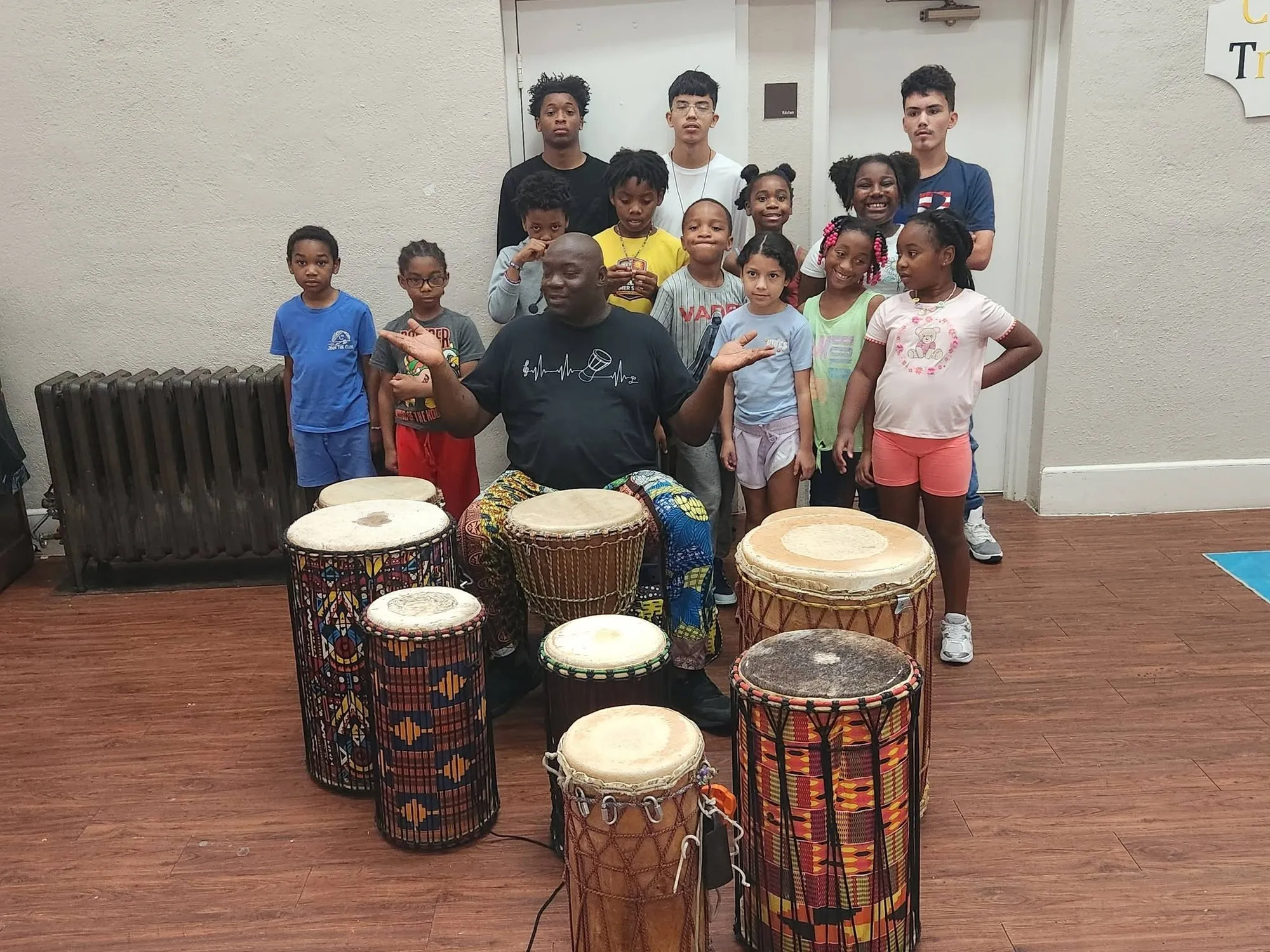 Instructor with djembe drums surrounded by SYP kids at the after-school program
